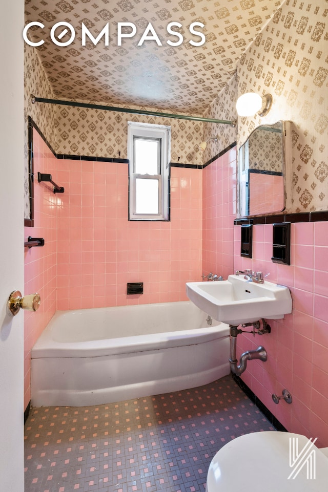 bathroom featuring toilet, a wainscoted wall, a sink, tile walls, and wallpapered walls