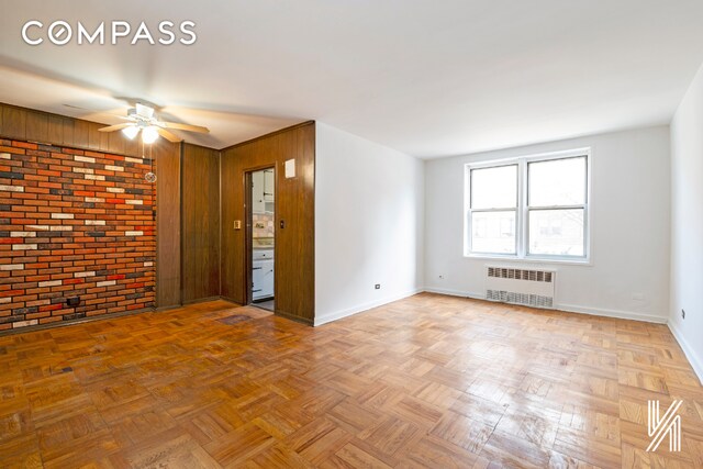 empty room featuring ceiling fan, radiator heating unit, brick wall, light parquet flooring, and wood walls