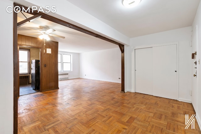 empty room with radiator heating unit, ceiling fan, wooden walls, beamed ceiling, and baseboards