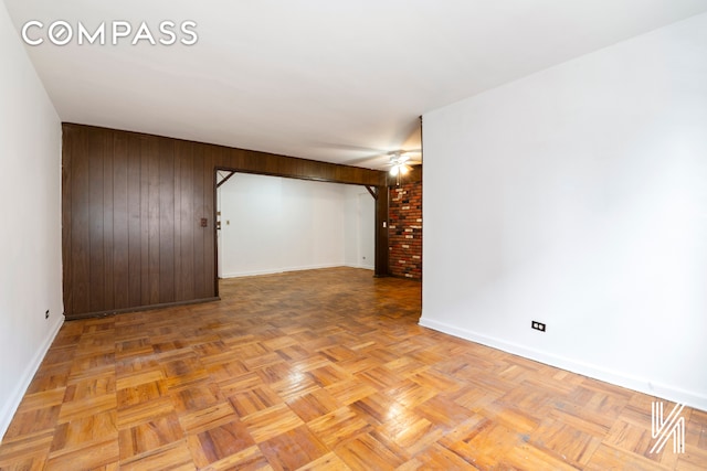 spare room featuring wood walls, baseboards, and a ceiling fan