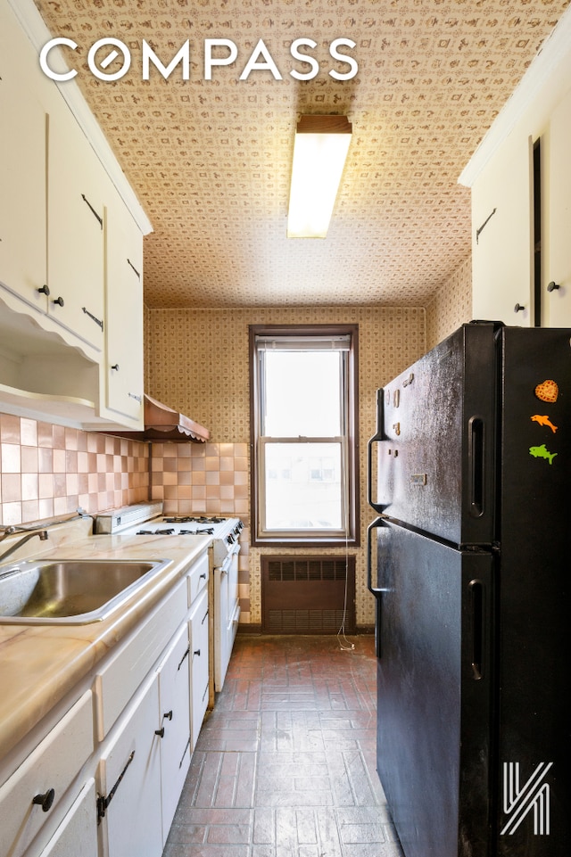 kitchen featuring white range with gas stovetop, freestanding refrigerator, light countertops, white cabinetry, and a sink