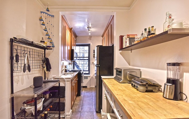 kitchen with crown molding, dark tile patterned floors, butcher block counters, appliances with stainless steel finishes, and open shelves