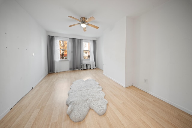 empty room featuring baseboards, light wood-style floors, a ceiling fan, and radiator