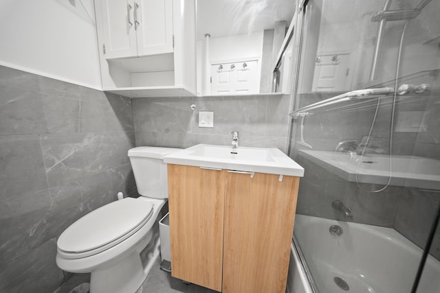 bathroom featuring toilet, enclosed tub / shower combo, tile walls, and vanity