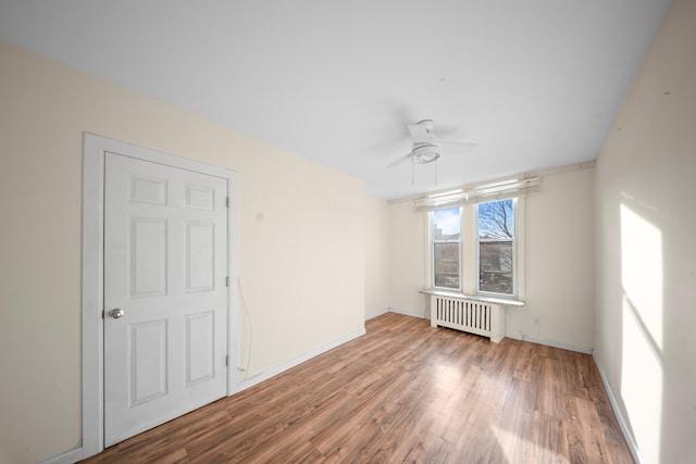 empty room with radiator, ceiling fan, baseboards, and wood finished floors