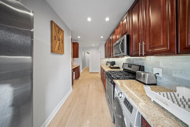 kitchen featuring light hardwood / wood-style floors, appliances with stainless steel finishes, backsplash, light stone countertops, and washer / clothes dryer