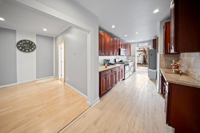 kitchen with decorative backsplash, appliances with stainless steel finishes, light stone counters, and light hardwood / wood-style floors