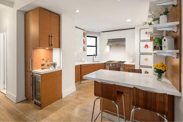 kitchen with tasteful backsplash, stainless steel range, light hardwood / wood-style floors, white cabinets, and exhaust hood