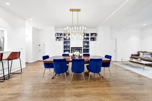 dining area featuring light wood-type flooring, built in features, and a notable chandelier