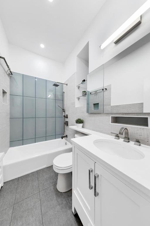 full bathroom featuring tile walls, vanity, tiled shower / bath combo, tile patterned flooring, and toilet