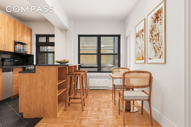 kitchen with kitchen peninsula, stainless steel dishwasher, a kitchen bar, and light parquet flooring