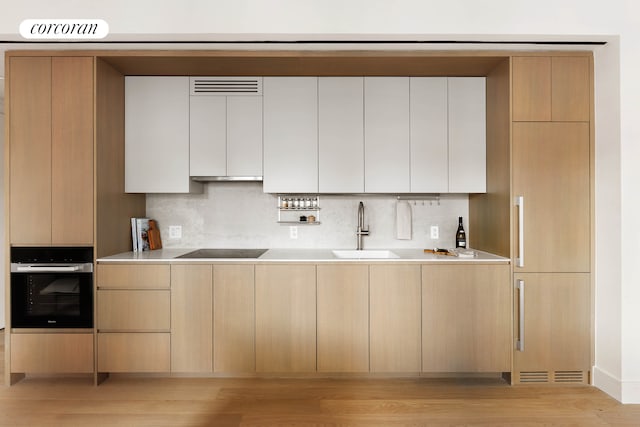 428 W 19th St Unit 8D, New York City, NY 10011 - kitchen with black appliances, light brown cabinetry, decorative backsplash, light wood-style floors, and modern cabinets