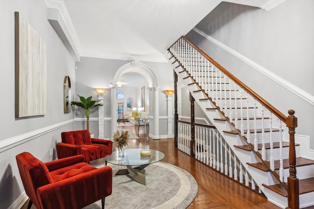 interior space featuring arched walkways, ornamental molding, wood finished floors, stairs, and ornate columns