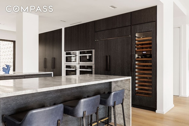 kitchen with wine cooler, a breakfast bar area, stainless steel double oven, and light wood-type flooring