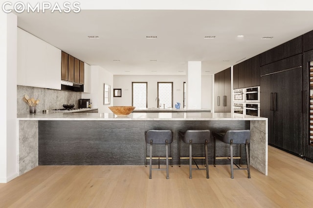 kitchen with white cabinetry, backsplash, a kitchen breakfast bar, kitchen peninsula, and light wood-type flooring