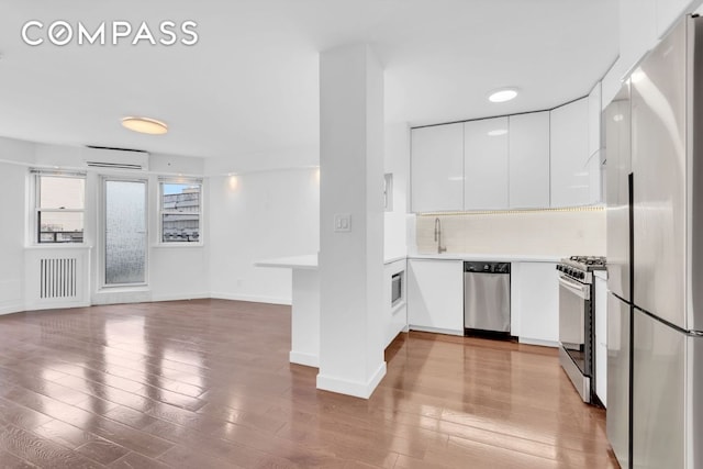 kitchen with an AC wall unit, radiator, white cabinetry, stainless steel appliances, and light hardwood / wood-style flooring