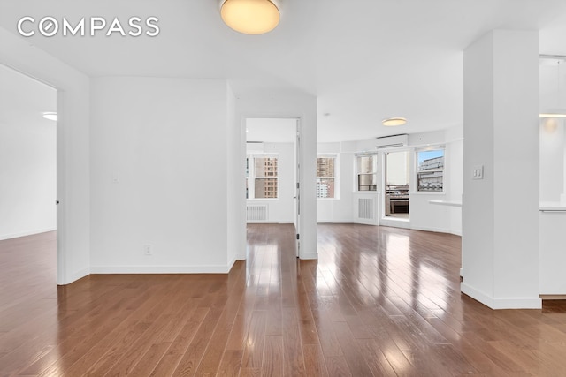 unfurnished living room with a wall unit AC, wood finished floors, visible vents, and baseboards