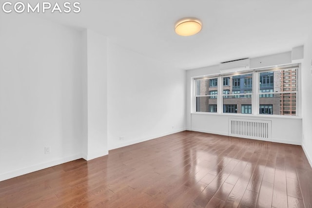 unfurnished room featuring a wall mounted AC, radiator heating unit, and hardwood / wood-style flooring