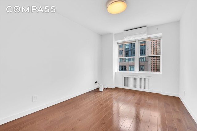 spare room with visible vents, baseboards, wood finished floors, and a wall mounted air conditioner