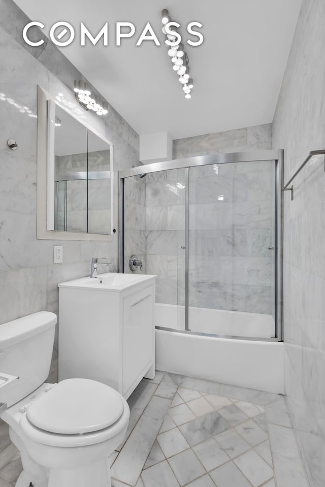 bathroom with marble finish floor, shower / bath combination with glass door, tile walls, toilet, and vanity