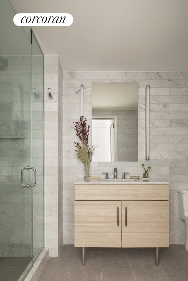 bathroom with tile patterned flooring, toilet, vanity, tile walls, and a shower stall