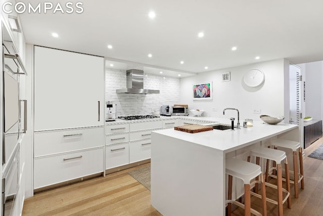 kitchen featuring stainless steel gas stovetop, a center island with sink, sink, white cabinets, and wall chimney exhaust hood