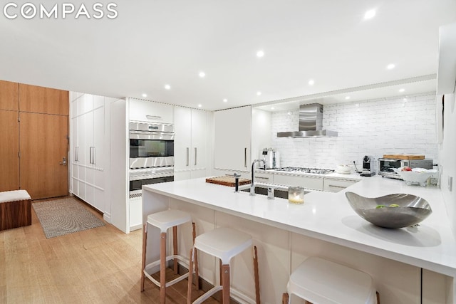 kitchen featuring appliances with stainless steel finishes, decorative backsplash, wall chimney exhaust hood, white cabinets, and a breakfast bar