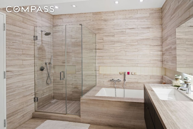 full bath featuring a stall shower, vanity, tile walls, and a bath