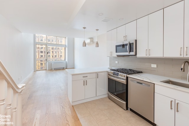 kitchen with sink, appliances with stainless steel finishes, decorative backsplash, white cabinets, and decorative light fixtures