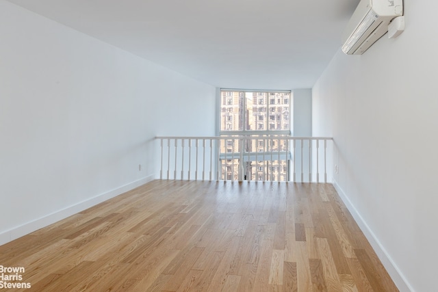 spare room featuring expansive windows, a wall mounted air conditioner, and light hardwood / wood-style floors