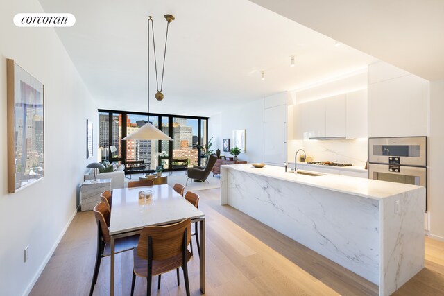 kitchen with white cabinetry, tasteful backsplash, an island with sink, pendant lighting, and light hardwood / wood-style floors