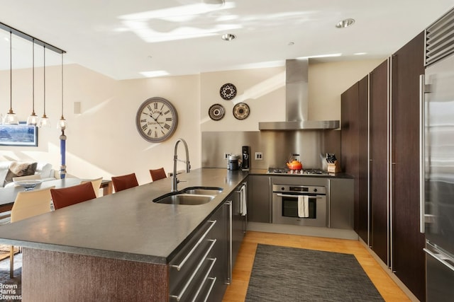 kitchen with wall chimney range hood, stainless steel appliances, sink, kitchen peninsula, and dark brown cabinets