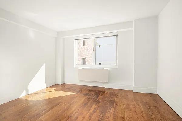 spare room with wood finished floors, baseboards, and radiator