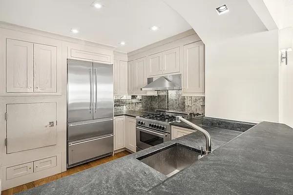 kitchen featuring premium appliances, a sink, under cabinet range hood, white cabinetry, and decorative backsplash