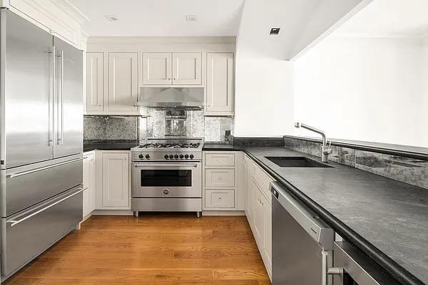 kitchen featuring premium appliances, under cabinet range hood, a sink, dark countertops, and white cabinetry