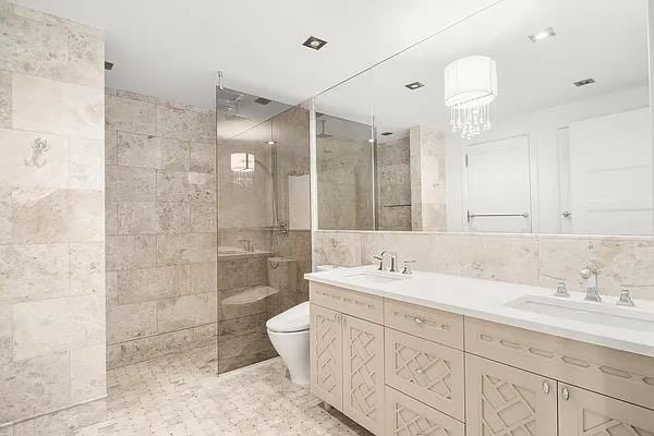 full bathroom with tile walls, a walk in shower, toilet, double vanity, and a chandelier