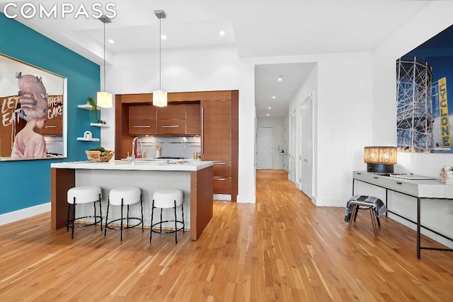 kitchen featuring sink, hanging light fixtures, light hardwood / wood-style flooring, a center island with sink, and a breakfast bar area