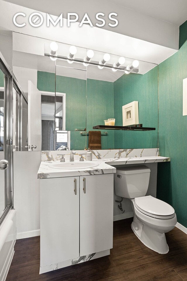 bathroom with toilet, wood finished floors, baseboards, and bath / shower combo with glass door