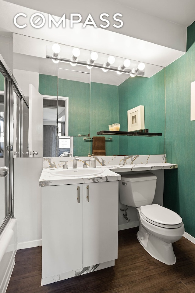 full bath with toilet, wood finished floors, shower / bath combination with glass door, baseboards, and vanity