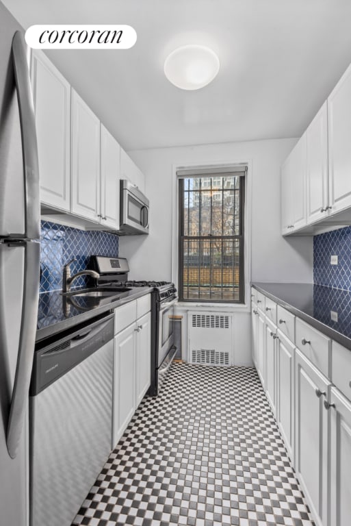 kitchen with radiator, sink, backsplash, stainless steel appliances, and white cabinets