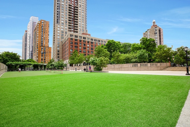 view of community featuring a view of city, a lawn, and fence