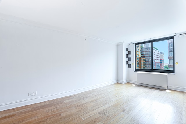 spare room with ornamental molding, baseboards, and wood finished floors