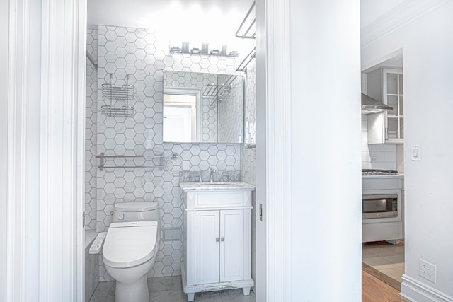 bathroom with tile walls, toilet, a tile shower, vanity, and tile patterned floors