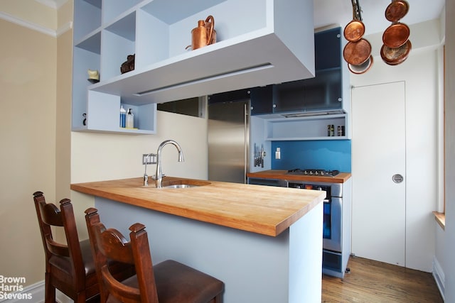 kitchen with a sink, butcher block counters, stainless steel built in fridge, and open shelves