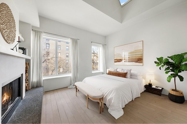 bedroom featuring a skylight, wood-type flooring, and a lit fireplace