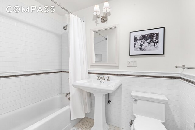 full bath featuring tile walls, a wainscoted wall, shower / bathtub combination with curtain, and toilet