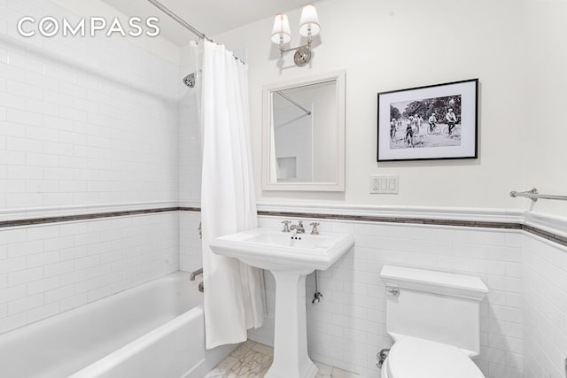 full bath featuring marble finish floors, shower / tub combo with curtain, toilet, a wainscoted wall, and tile walls
