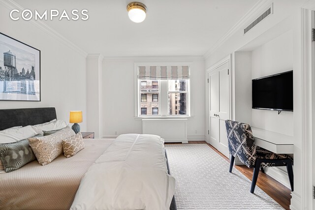 bedroom with baseboards, wood finished floors, visible vents, and crown molding