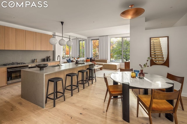 kitchen with tasteful backsplash, pendant lighting, sink, light wood-type flooring, and wall oven