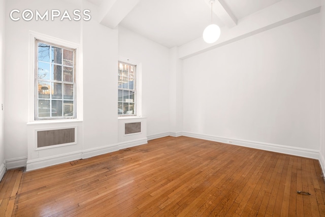 spare room featuring light wood finished floors, beam ceiling, and baseboards